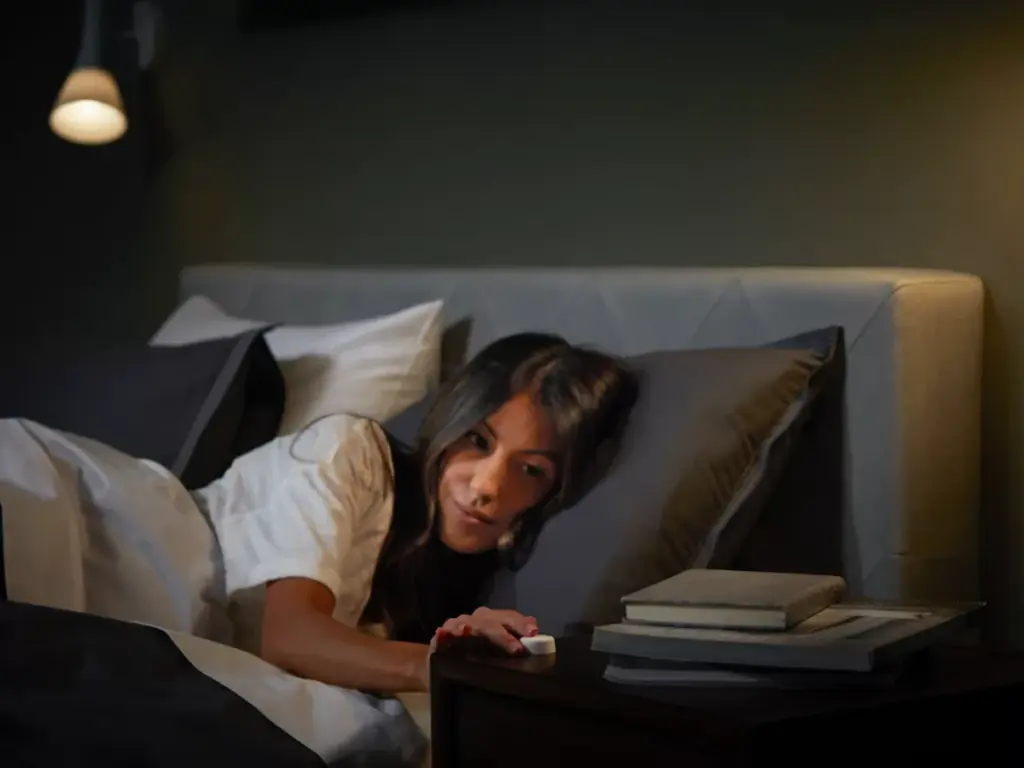 Frau schaltet Philips Hue Lampe im Schlafzimmer per Smart Button vom Bett aus